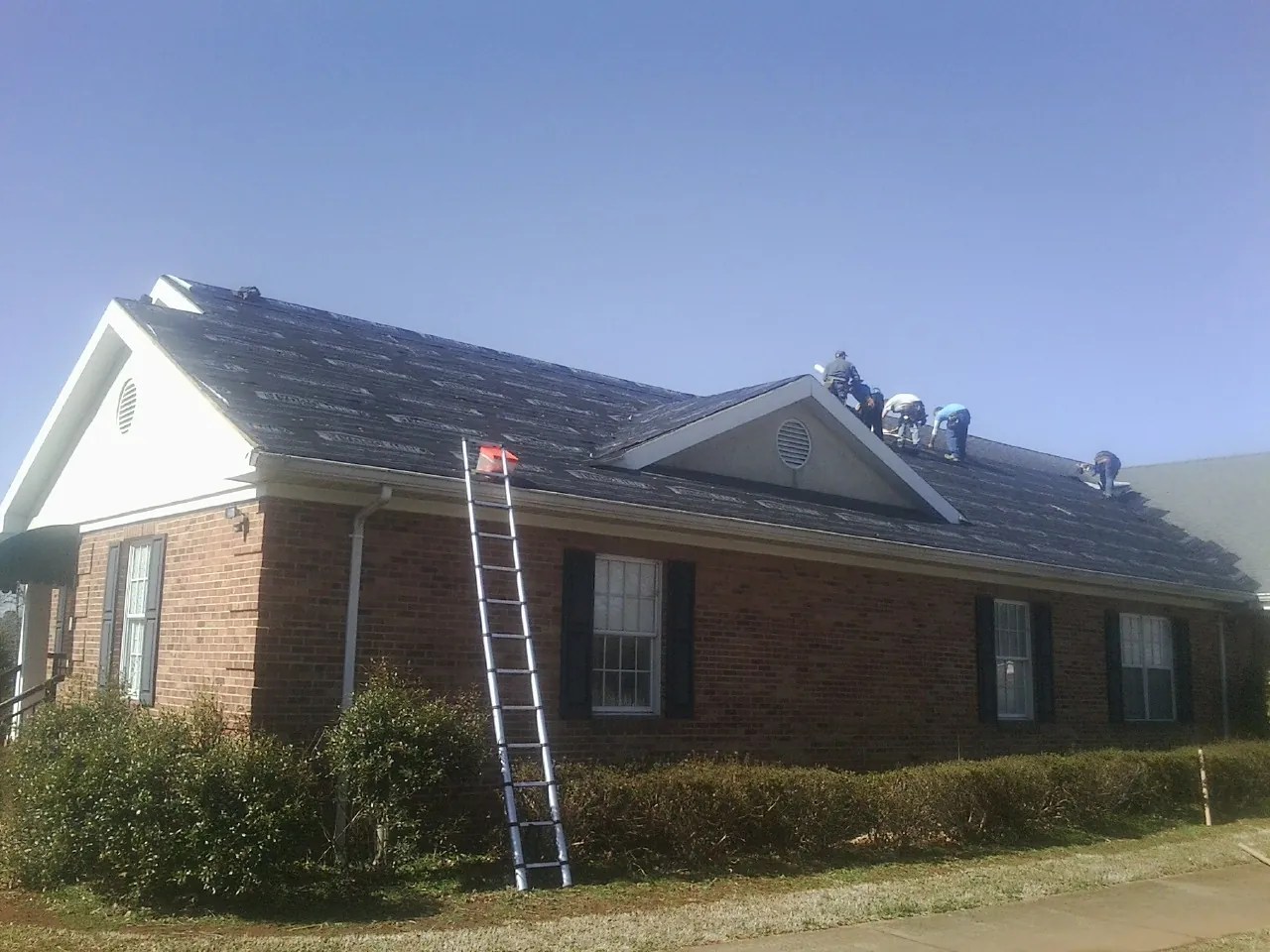 Crew tearing shingles off a brick ranch roof with a ladder set — Metal Roof Repair work by our crew in Chunchula