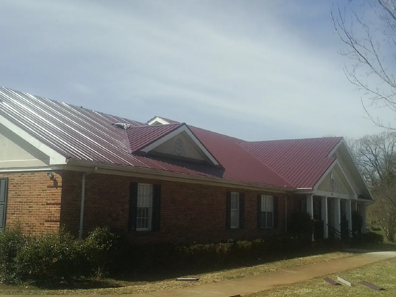 Red metal roof with gabled entries on a long brick building, from a Hail Damage Roof Repair job in Chunchula