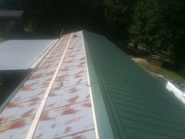 Old rusted panels beside newly installed green metal roofing — Wind Damage Roof Repair by Roofing Brothers in Chunchula