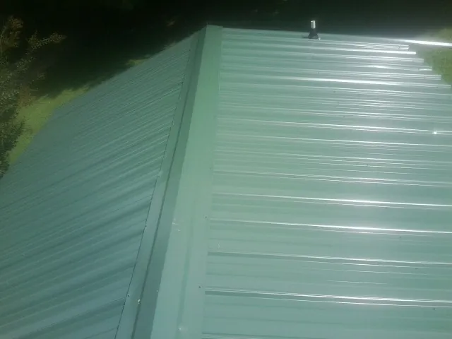 New green metal panels meeting at the ridge of a roof — Flat Roof Repair work by our crew in Chunchula