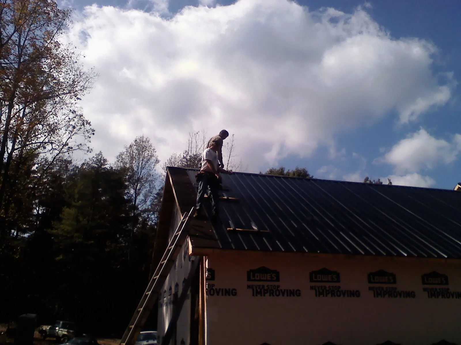 Roofer fastening dark metal panels high against a cloudy sky, from a Roof Inspection job in Chunchula